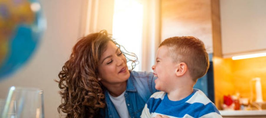 Kind mother helping her son doing homework in kitchen. Mother Helping Son With Homework At Table. Children's creativity. Portrait of smiling mother helping son with homework in kitchen at home